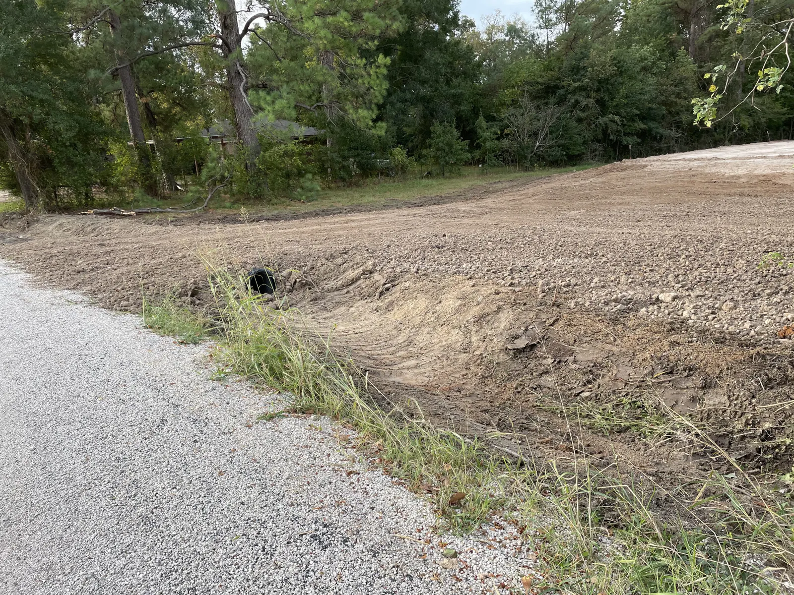 Fresh gravel driveway beside a graded slope with a new culvert pipe