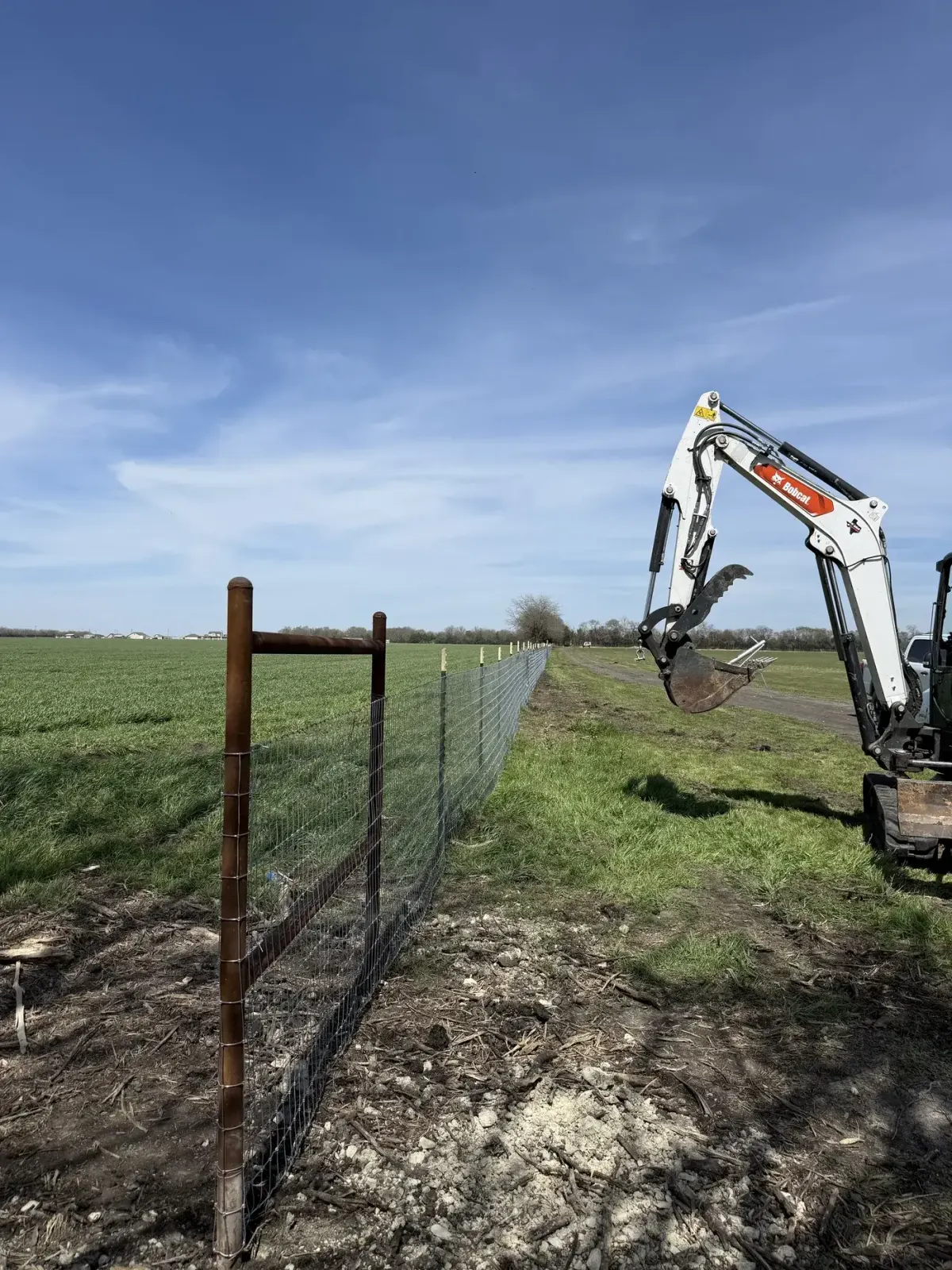 Bobcat mini excavator setting posts on a new pasture fence