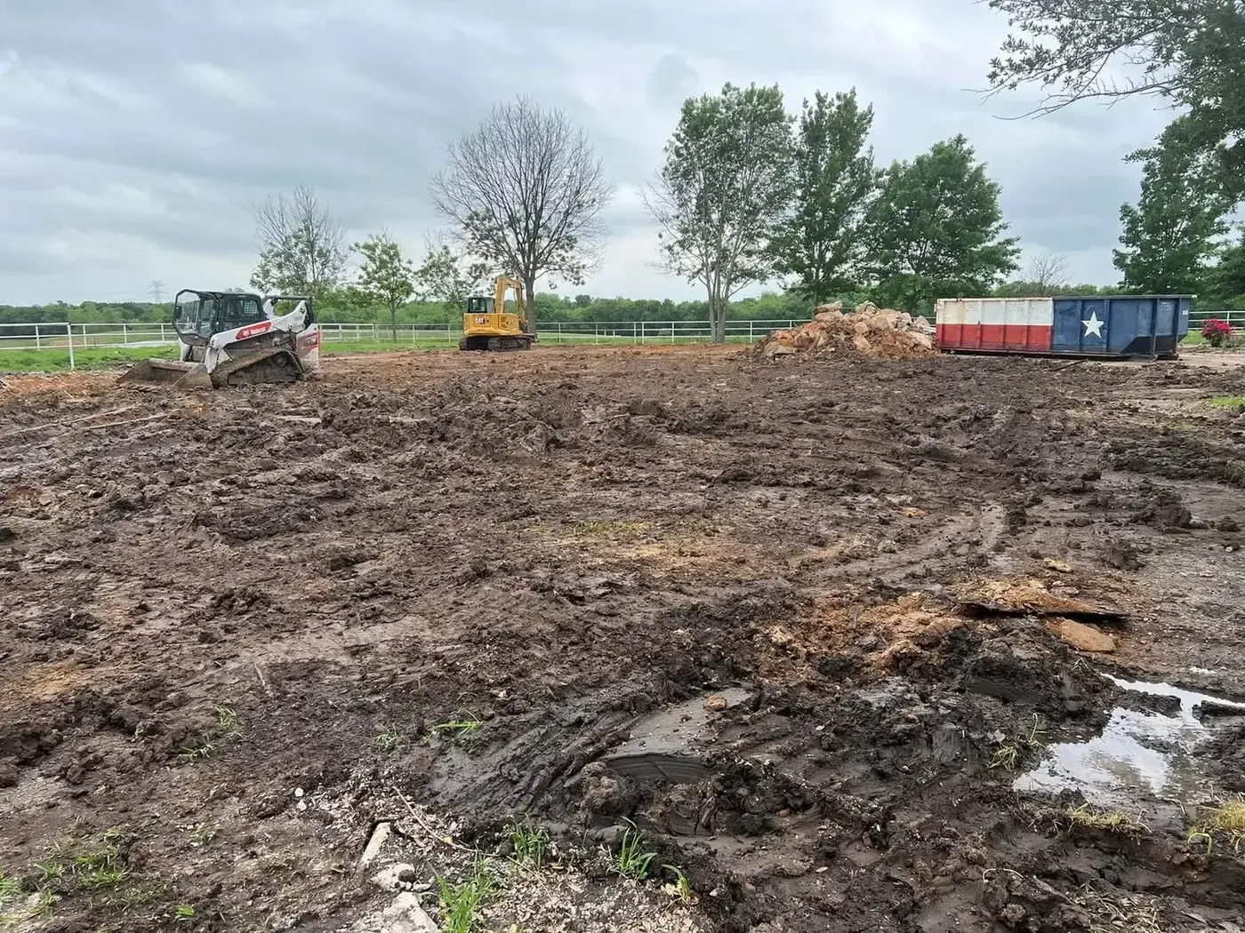 Skid steer clearing demolition debris beside a roll-off dumpster