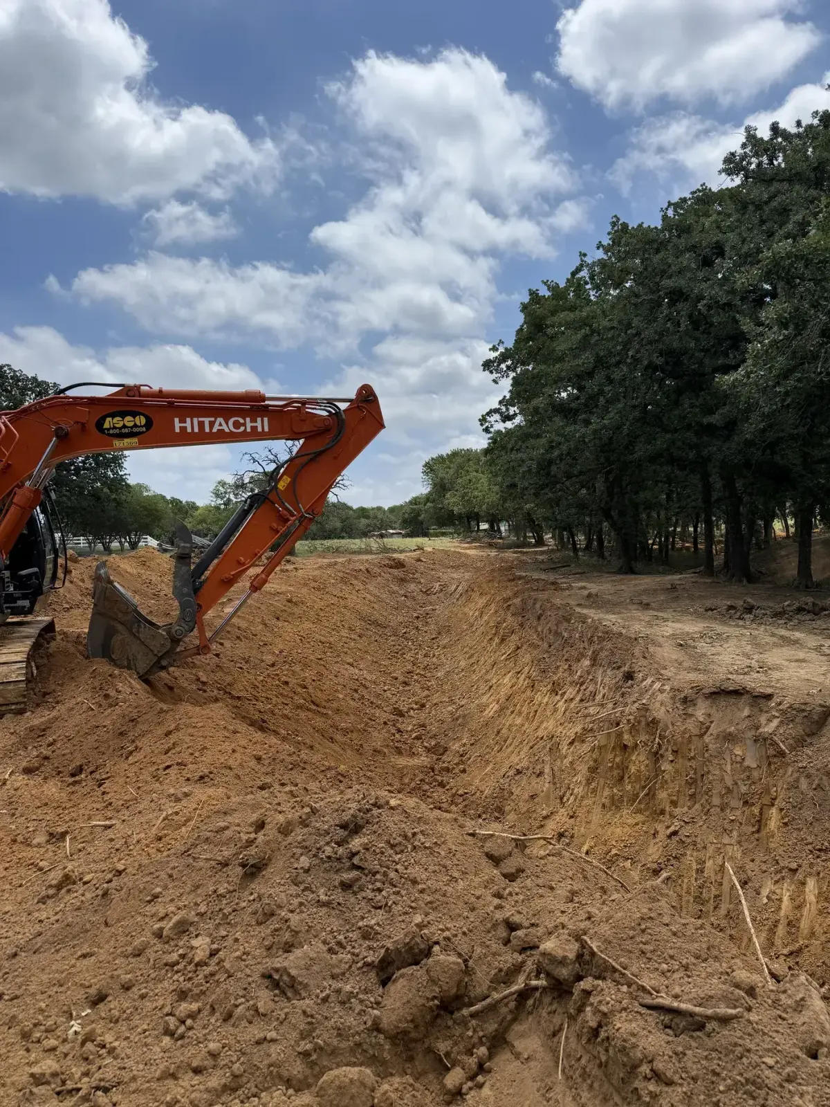3L Land Services Hitachi excavator digging a trench in red clay
