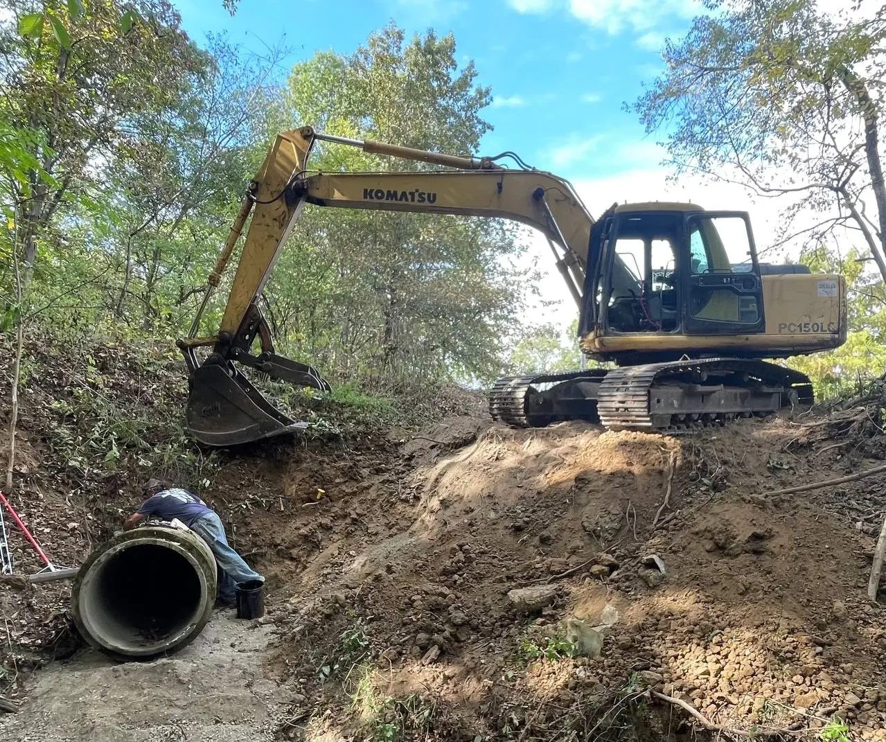 Komatsu excavator setting a new culvert pipe in a ditch
