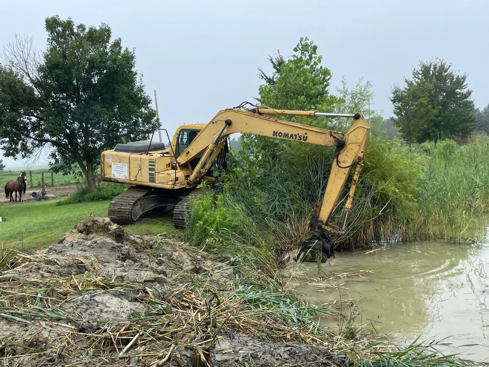 Komatsu excavator pulling a root mat out of a pond during a cleanout in Urbana, IL