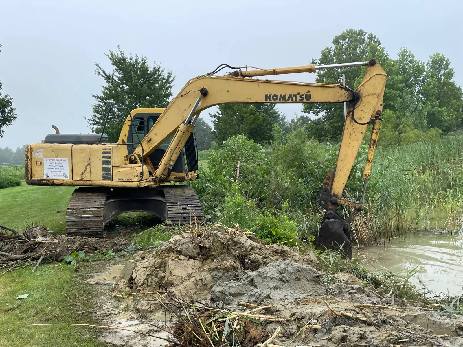 Komatsu excavator pulling cattails and muck from a pond bank in Urbana, IL
