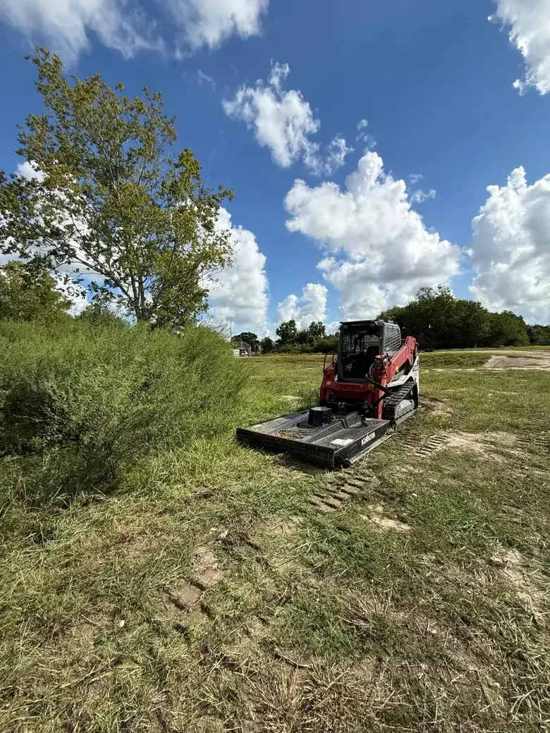 Skid steer with a brush cutter working an open field in West Houston
