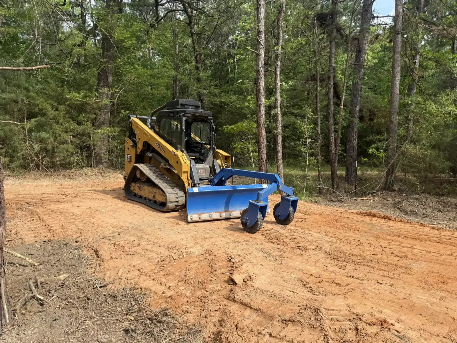 Cat track loader with a box blade grading red clay on a cleared site