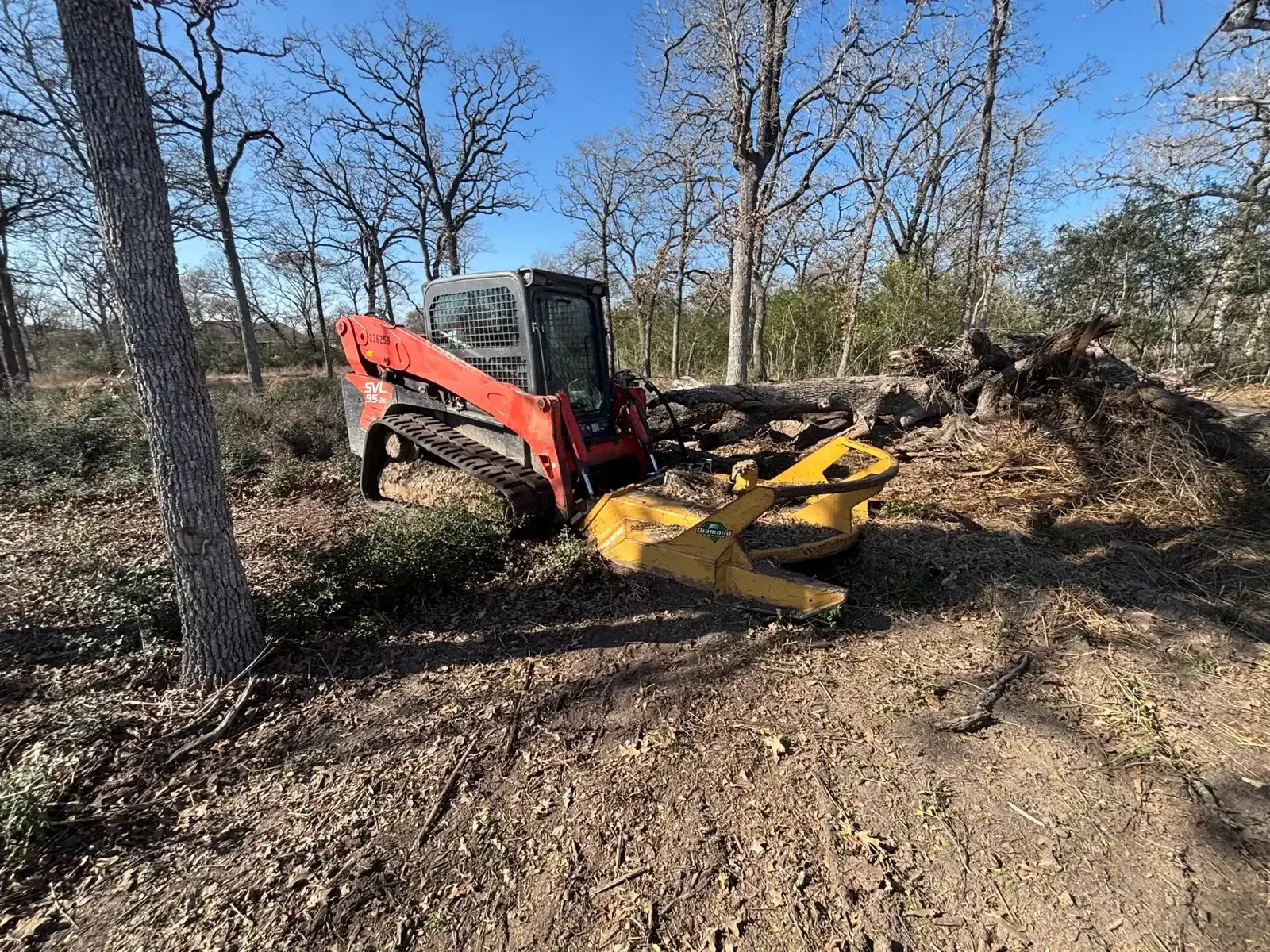 Track loader with a mulching head working through brush and downed limbs