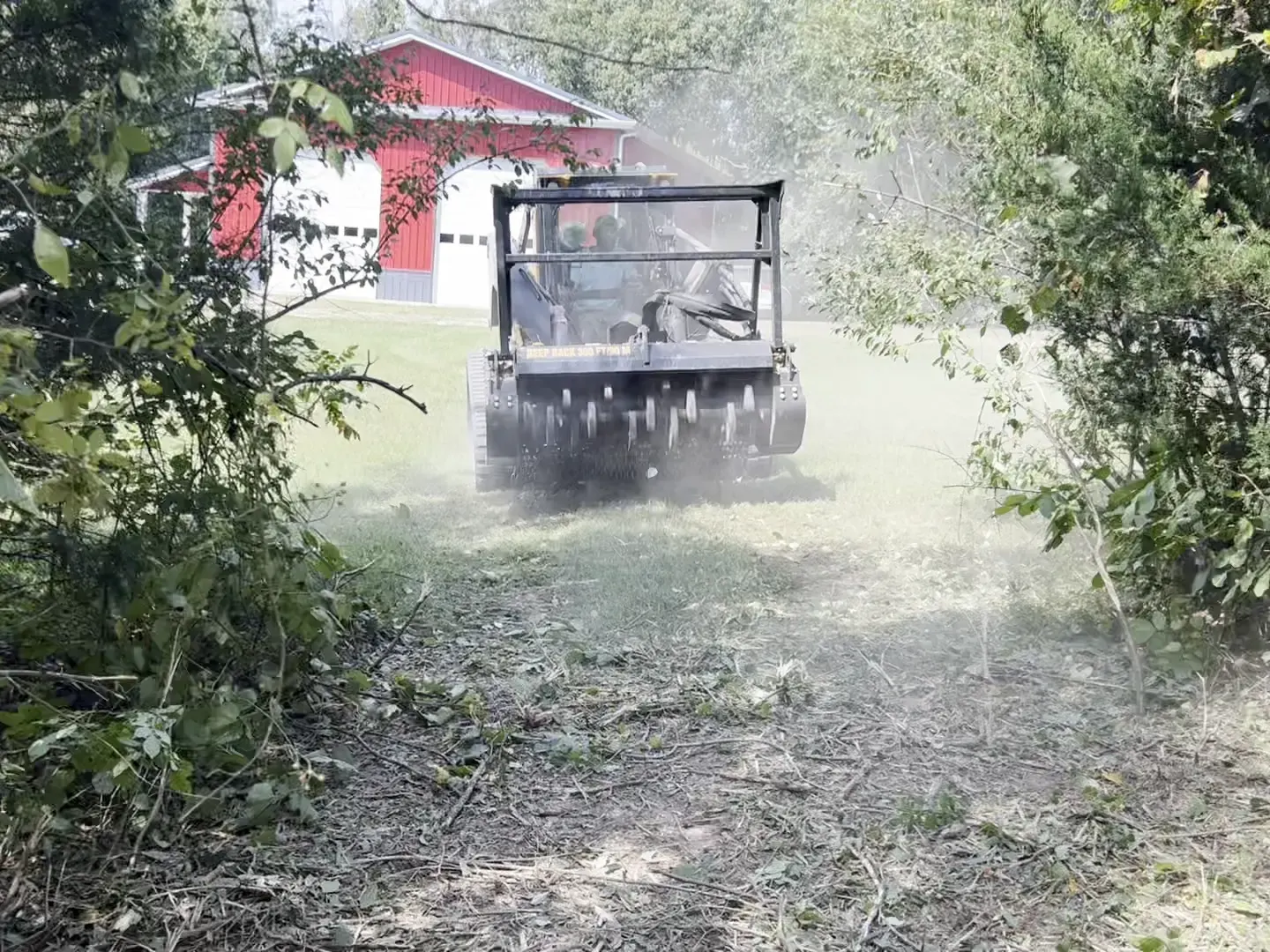 Mulcher clearing brush toward a red barn