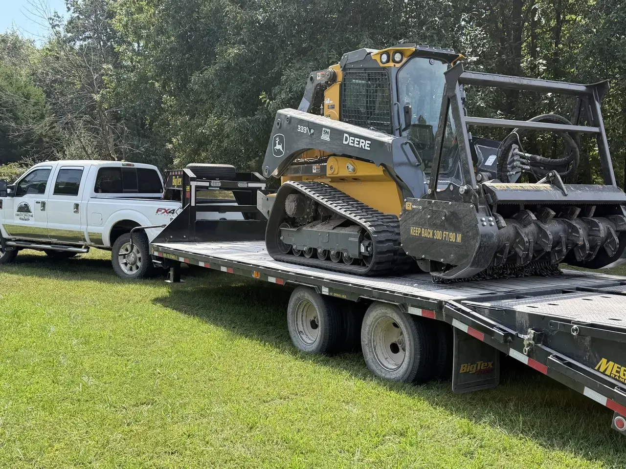 Track loader with mulching head loaded on a gooseneck trailer behind the company truck