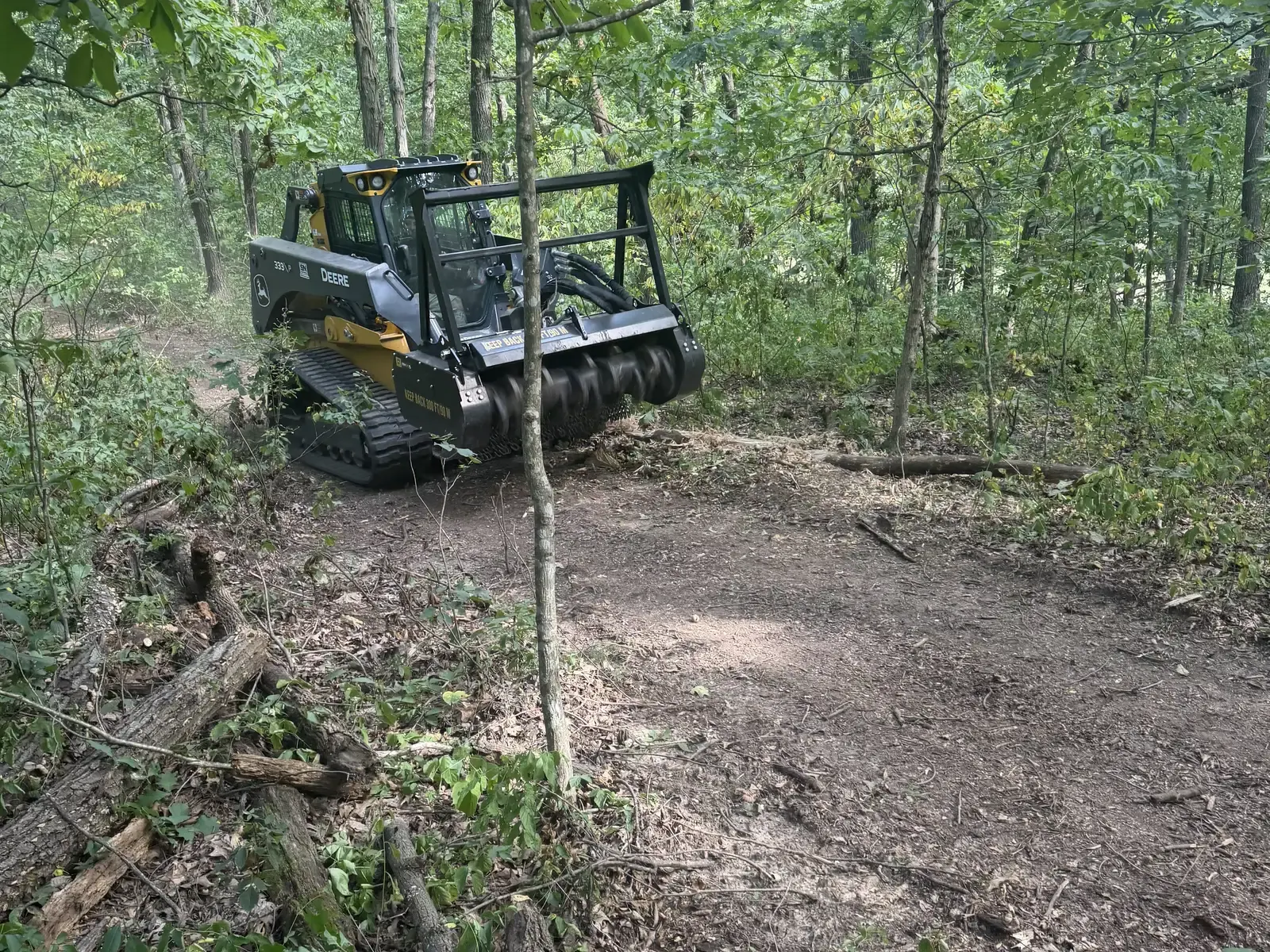 Track loader with mulching head opening a trail through hardwood timber