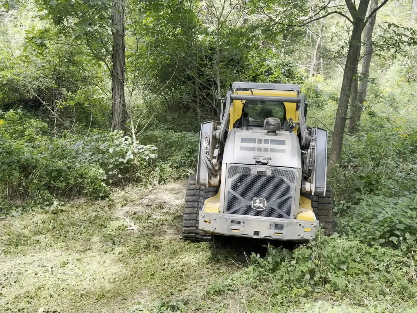 John Deere track loader in a lane cleared through brush