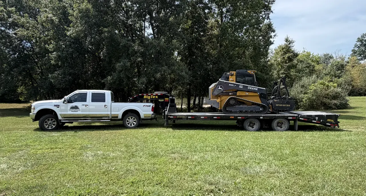 Company pickup, gooseneck trailer and forestry mulcher parked on grass