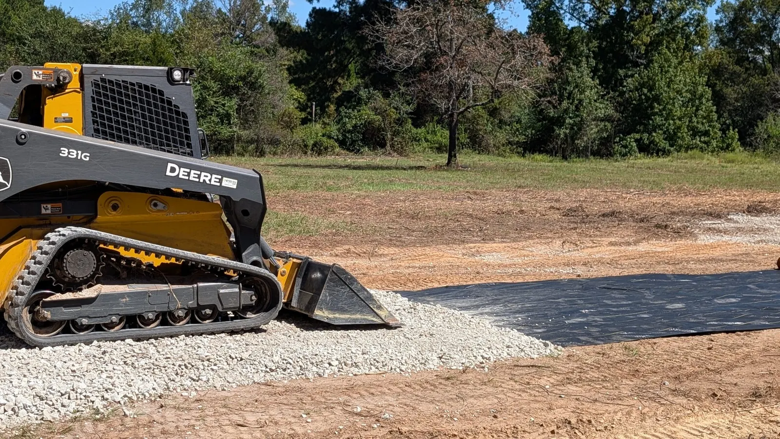 John Deere track loader spreading gravel over fabric for a driveway