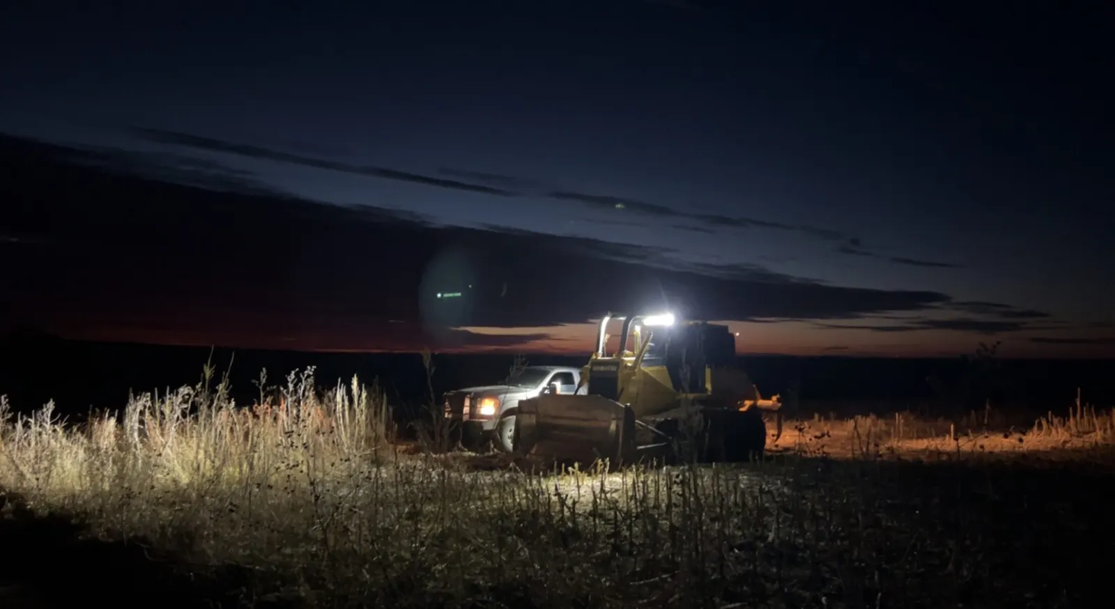 Dozer working under lights in a field at dusk