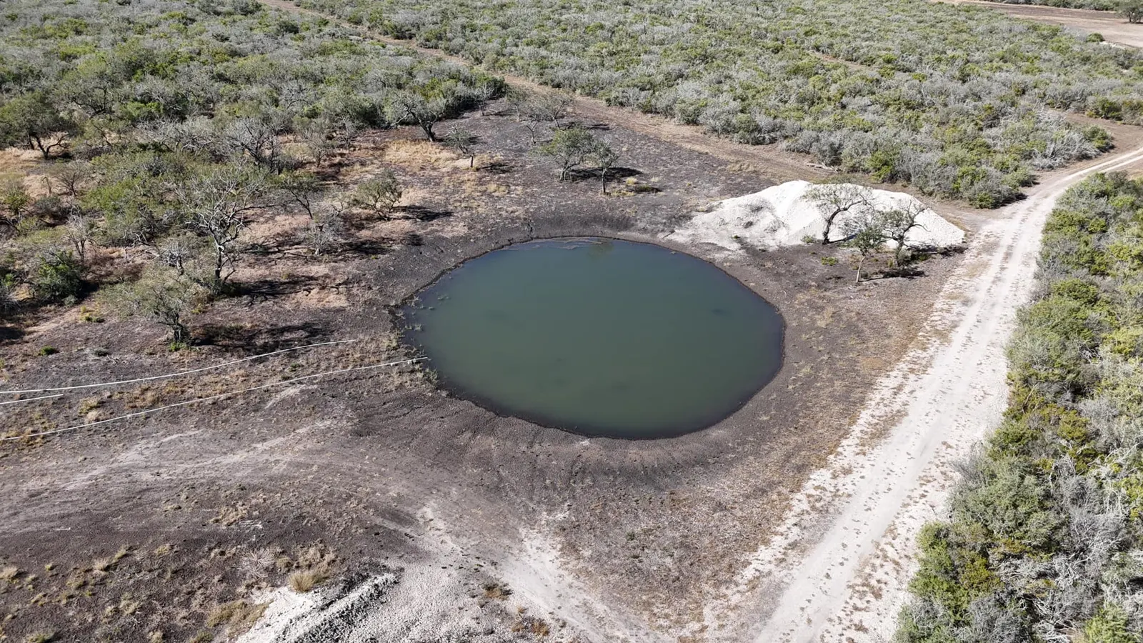 Aerial view of a stock pond surrounded by cleared brush land
