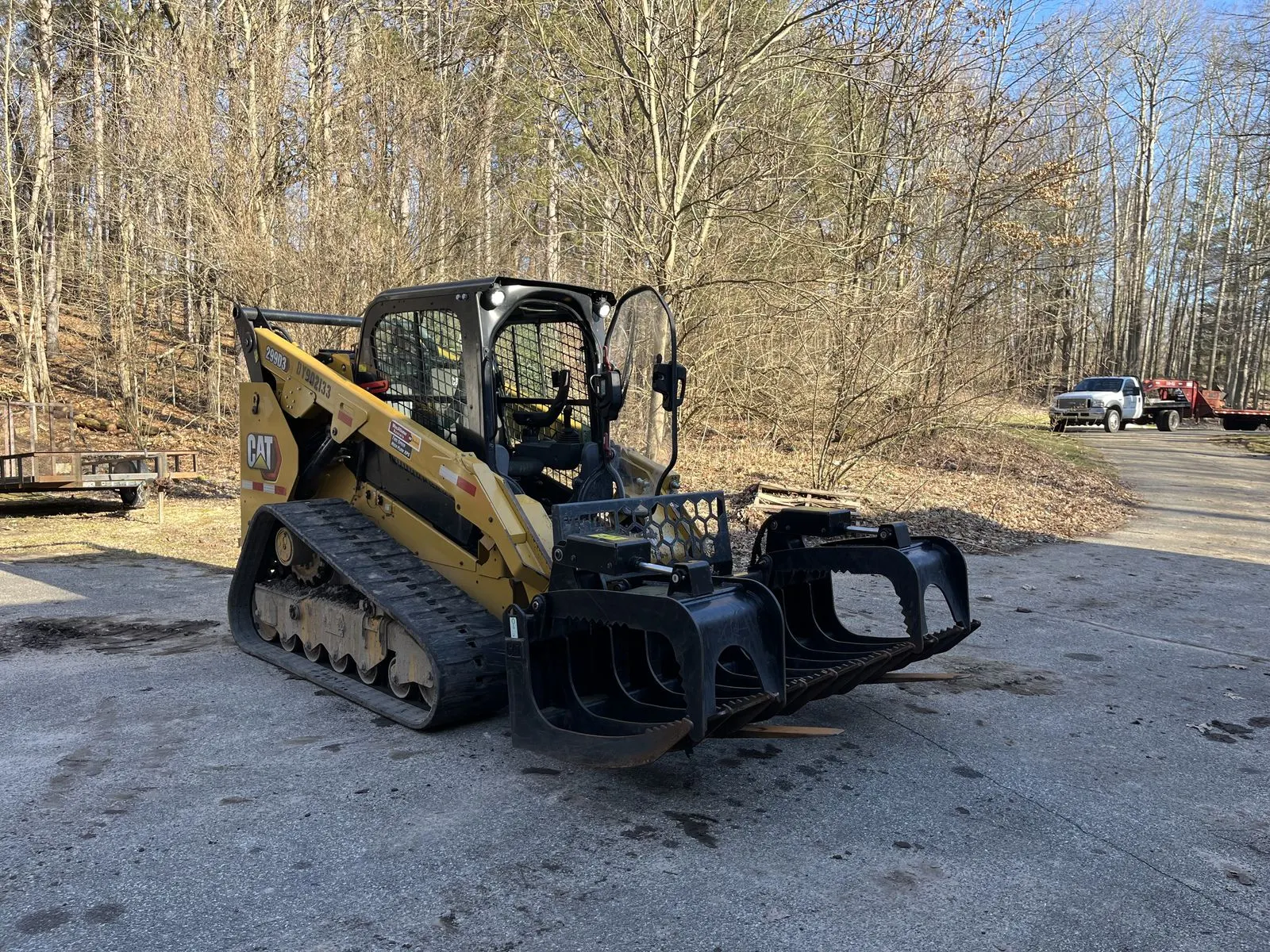Compact track loader with a grapple attachment on a gravel drive